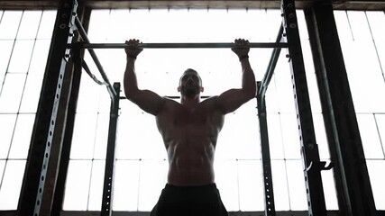 A powerful, muscular male figure in detailed silhouette performs challenging pull-ups on a black power rack, backlit by industrial windows with soft bokeh. Concept of strength training and dedication - Powered by Adobe
