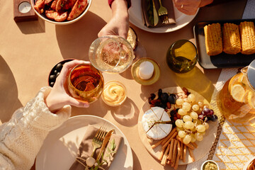 Senior woman and girl toasting with glasses over festive table setting, sharing assorted cheese, grapes, corn, and appetizers, enjoying outdoor meal together