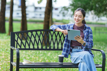 Young asian woman enjoying digital content on tablet in park