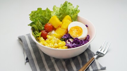 A bowl of salad with corn, egg, mango, tomato, lettuce, red cabbage isolated on white background