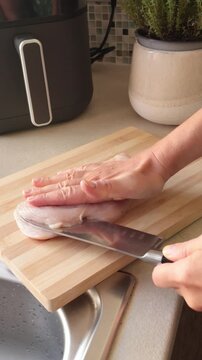 Anonymous person cut chicken breast lengthwise with knife on kitchen table at home. Farm products, food, recipes. Protein and healthy eating.