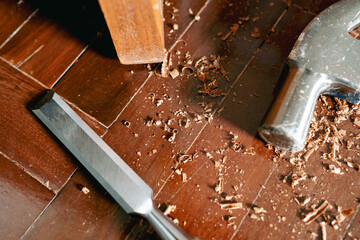 Woodworker's equipment, which is a chisel and hammer, is on a wooden floor with sawdust.
