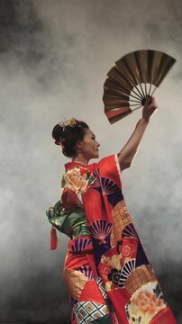 Japanese Geisha In Red Embroidered Kimono With Golden Fan Performing Graceful Turn In Studio Smoke Creating Flowing Motion Of Sleeves Symbolizing Art Of Movement And Timeless Japanese Elegance