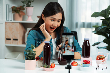 Smiling young beautiful Asian reviewing tasty mixed strawberry and cherry juice detox drinks, showing healthy product to promote for special promotion selling on social media online record. Stratagem.
