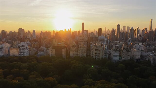 Breathtaking Drone shot over New York City Central Park at sunrise with colorful trees at full, morning light scene of cityscape, tall building stands agains the sun. New York, USA