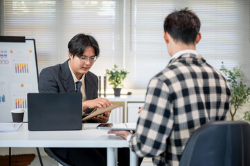 Glasses asian businessman holding document envelope talking to employee at working table in office.
