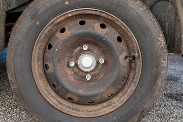 Tire with a black rim and a white center. The tire is old and worn. The rim is rusted and has holes in it