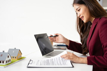 Real estate agent professional reviewing documents while working on a laptop.