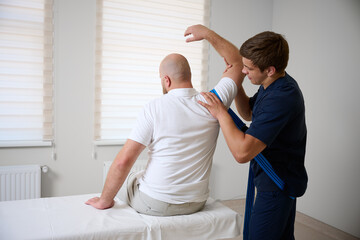 Chiropractor adjusting male patient’s shoulder in clinic. Physiotherapist performing manual therapy to relieve pain, improve mobility, support rehabilitation after injury or musculoskeletal disorder.
