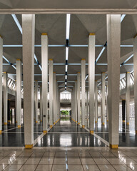 Masjid Negara, aka National Mosque interior, Kuala Lumpur, Malaysia. Modern architectural design with repeating tiled columns, golden bases, reflective floors, and geometric skylit ceiling.