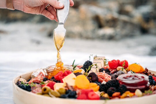 Honey being drizzled over a beachside charcuterie board.