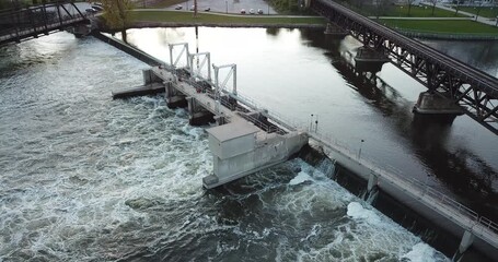 Aerial drone video of river water flowing over a hydro dam with two railroad bridges crossing the river.