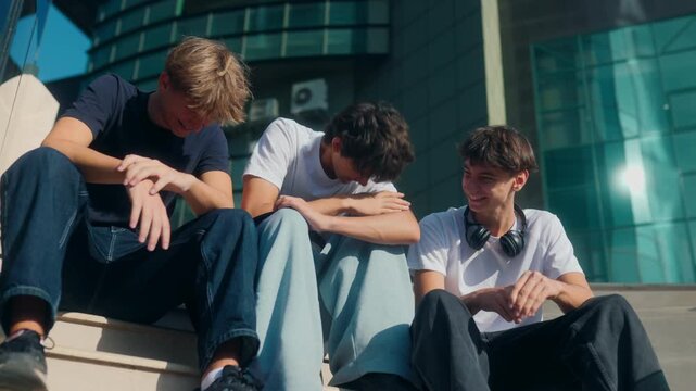 Three teenage boys laughing and chatting casually while sitting on stairs