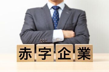 「赤字企業」と書かれたブロックと腕組みをするビジネスマン