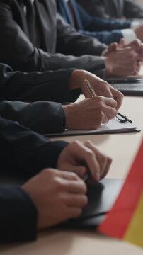 Vertical of politicians and diplomats seated at conference table with notepads and folders, focused on agenda during formal international discussion