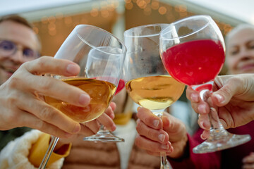 Group of diverse people clinking glasses outdoors, celebrating together, hands and faces partially visible, festive gathering