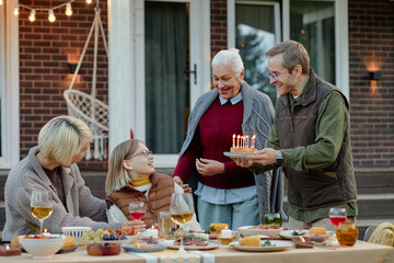 Caucasian middle aged man presenting birthday cake with candles to smiling Caucasian child,...