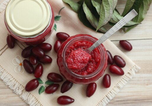 Homemade preserved  jam from Cornelian cherry dogwood, lat. Cornus mas macrocarpa,  in a jar. Also known as cornel or Cornelian cherry or European cornel. Fresh berries around on embroidered napkin.