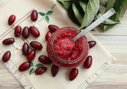 Homemade preserved  jam from Cornelian cherry dogwood, lat. Cornus mas macrocarpa,  in a jar. Also known as cornel or Cornelian cherry or European cornel. Fresh berries around on embroidered napkin.