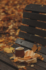 A brown coffee cup and a bun on a bench in an autumn park