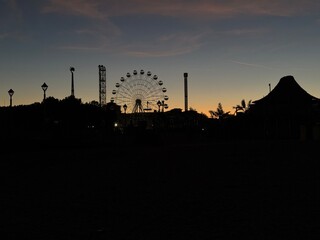 Evening view of amusement park at sunset with ferris wheel silhouette.