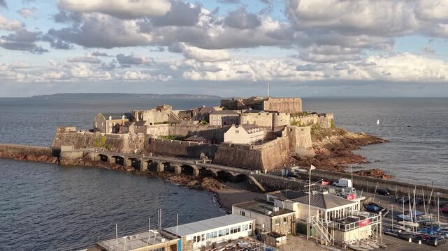 Close low circling drone footage of Castle Cornet St Peter Port Guernsey with interesting light and moody cloudy sky in afternoon sun