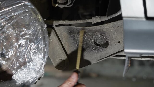 Lanolin rust protection being applied to flat structural piece with precision spray nozzle behind rear brake disc to guard against corrosion