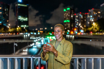 Woman smiling using smartphone on urban bridge at night