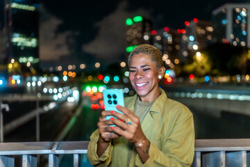 Woman smiling using smartphone on urban street at night
