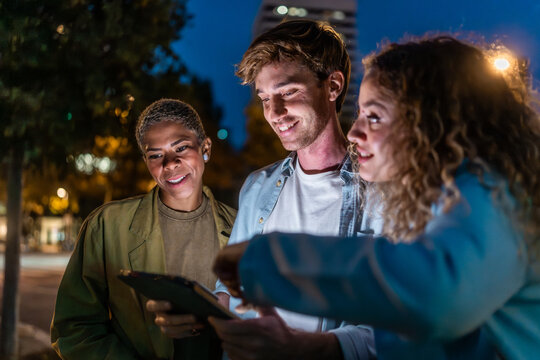 Diverse friends collaborating on tablet during night city outing