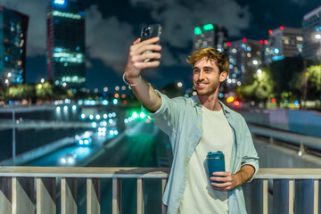 Young man taking selfie on city bridge at night