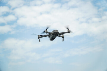 A modern gray drone ascends against a serene sky filled with fluffy white clouds, showcasing innovation and freedom. Captures aerial perspective, and modern technology in a single frame.