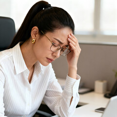 Businesswoman with headache holding her head while sitting at her desk in a bright office space