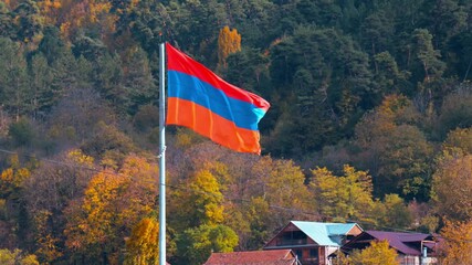 A Armenian flag with the colors red, white, and blue is flying in the air. The flag is on a pole in a forested area - Powered by Adobe