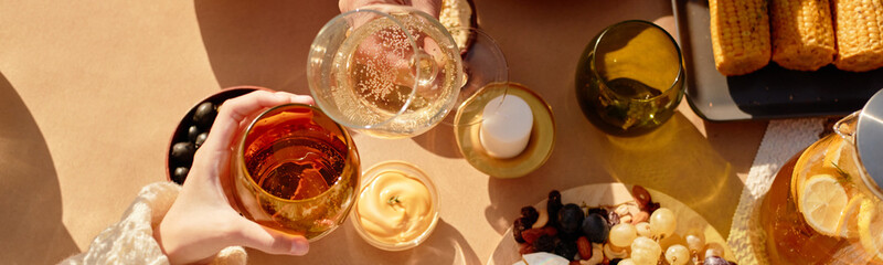 Unrecognizable people toasting with glasses of wine and fizzy drink over table set with snacks,...