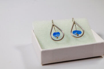 Silver earrings for pierced ears with blue stone mounted in a white box on a white background