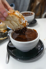 Hand dipping brioche pastry into hot chocolate drink