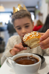 Boy wearing crown eating roscón de reyes with hot chocolate
