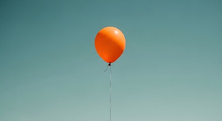 A single bright orange balloon floats serenely against a clear pale blue sky
