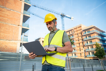 Construction engineer analyzing plans on laptop at building site