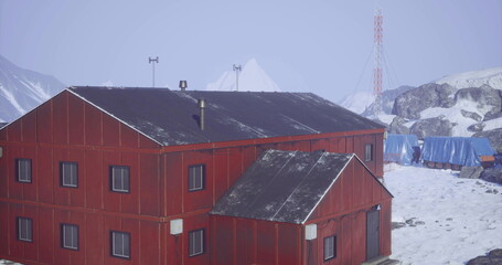 A red wooden research station stands amidst snow and rocky terrain with mountains in the background. Equipment is visible, indicating ongoing scientific activities in a remote area. © icetray