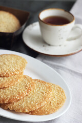 Sesame cookies in a white plate on the table, next to a cup of black tea