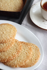 Sesame cookies in a white plate on the table, next to a cup of black tea