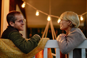 Middle aged Caucasian man smiling and talking with middle aged Caucasian woman leaning on wooden...
