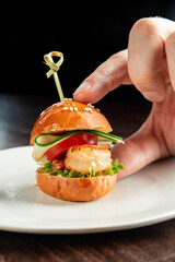 A hand holds a delicious slider featuring grilled shrimp, fresh tomato, cucumber, and lettuce on a...