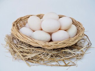 Several large duck eggs are placed in a wicker basket on a white background.