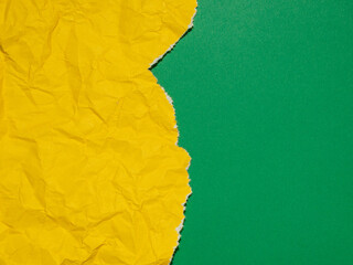 A bright yellow crumpled and torn paper against a solid green background.