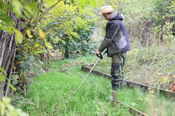 Country man working with an electric lawnmower in his yard
