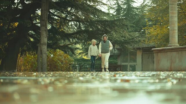 Two sisters are walking in a park in rain weather. The man is wearing a hoodie and the woman is wearing a white shirt