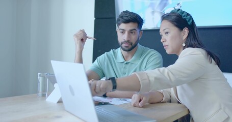 Collaborating woman and man examining laptop and tablet at office meeting table, with stylus papers
